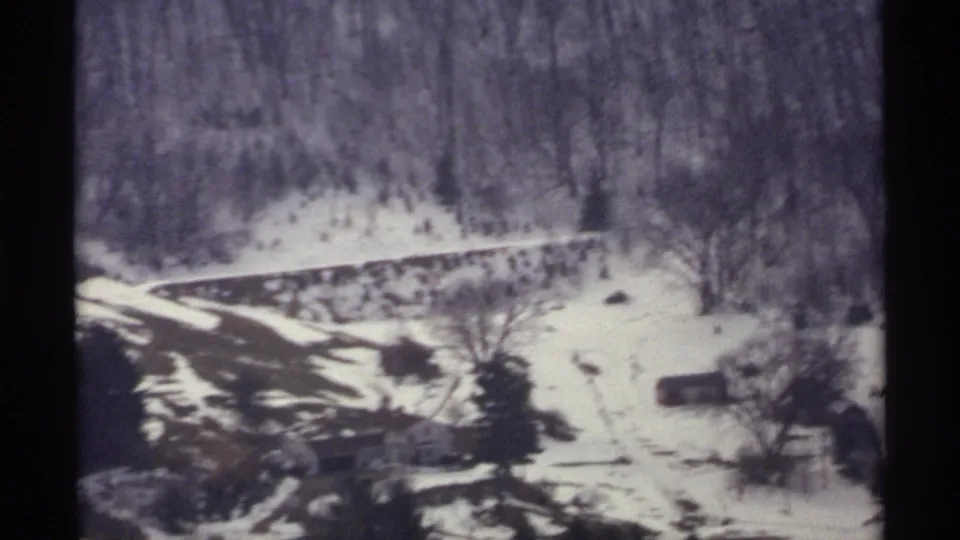 1971 La Crosse winter landscape frame showing snow patches, leafless trees, a curving road, and distant rural buildings below the hill.