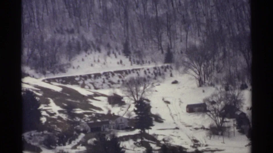Soft 8mm view of a La Crosse winter hillside with snow, a winding road, distant farm buildings, and dense bare woods.