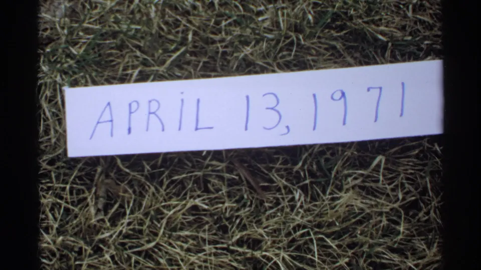 Close view of a handwritten April 13, 1971 card placed on grass in archival 8mm home-movie footage.