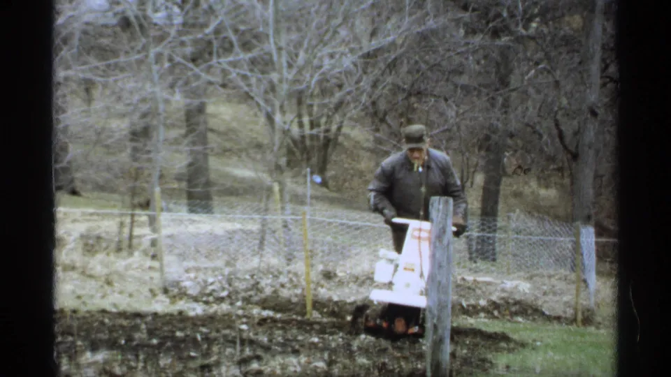 A front view shows the man operating the compact tiller in a 1971 Wisconsin backyard garden plot.