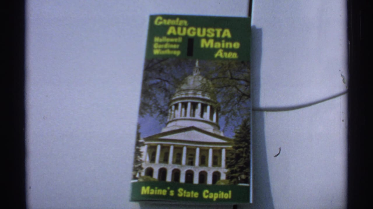 Green Greater Augusta Maine Area brochure on a pale wall, showing Maine's State Capitol.