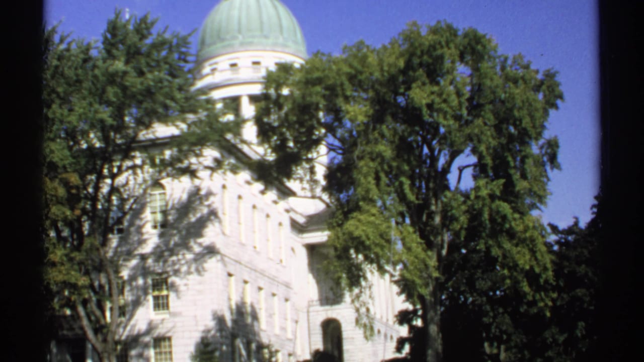 1971 Maine view of the white State Capitol building in Augusta, with its green dome rising behind trees.