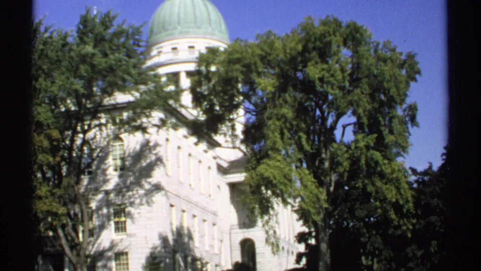 1971 Maine view of the white State Capitol building in Augusta, with its green dome rising behind trees.