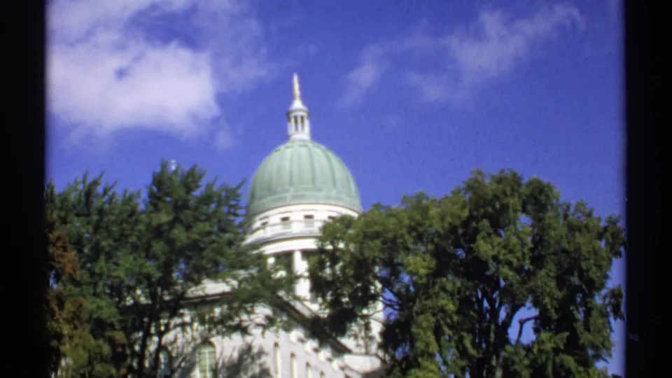1971 Maine home-movie view of a green-domed public building, with trees obscuring part of the white facade.