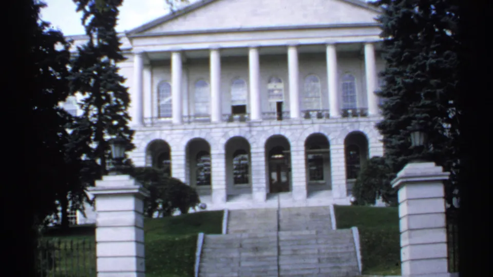 1971 Maine 8mm frame showing the front entrance of a white columned government building with stone steps and flanking pillars.