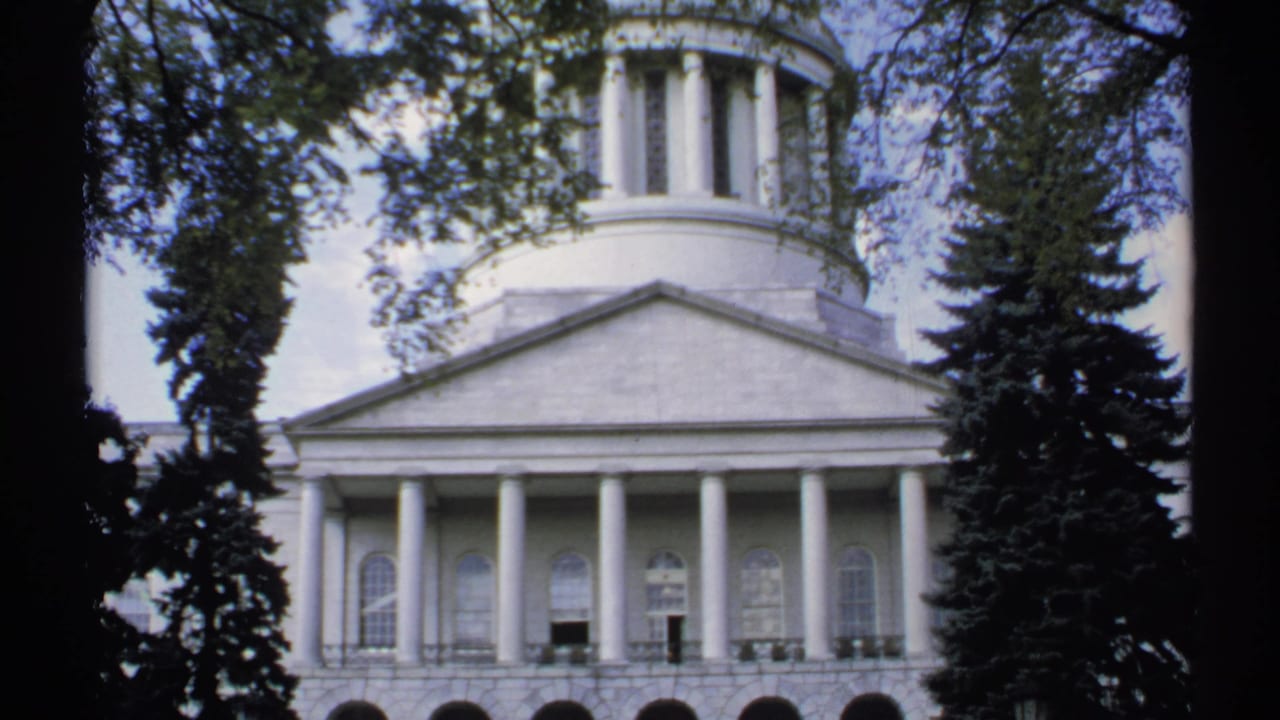 White columned building with cupola seen through trees.