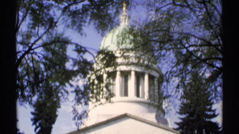 1971 Maine 8mm frame with a soft, handheld view of a white domed landmark partly hidden by trees.