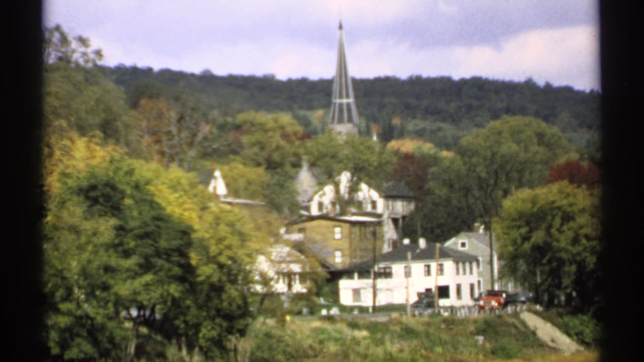 1971 Maine 8mm view of a small town with a church steeple rising above houses and autumn trees.