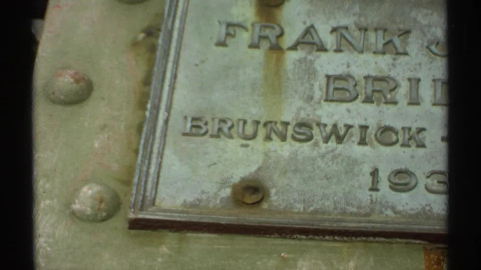 Close 8mm detail of a weathered metal plaque showing partial text including Frank J. Bridges and Brunswick.