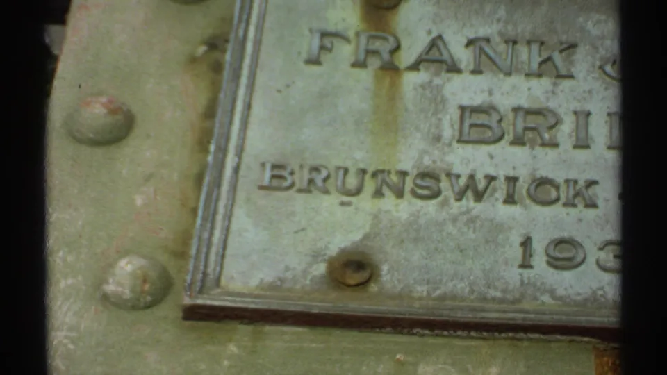 1971 Maine 8mm frame showing a weathered plaque with partial Frank J. Bridges and Brunswick text on a rusted green metal surface.