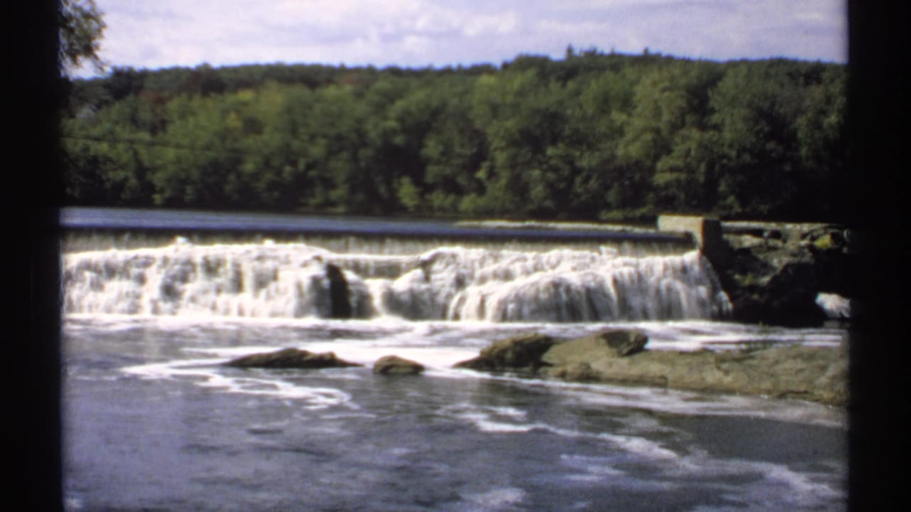 Water drops over a low dam into a rocky river channel.