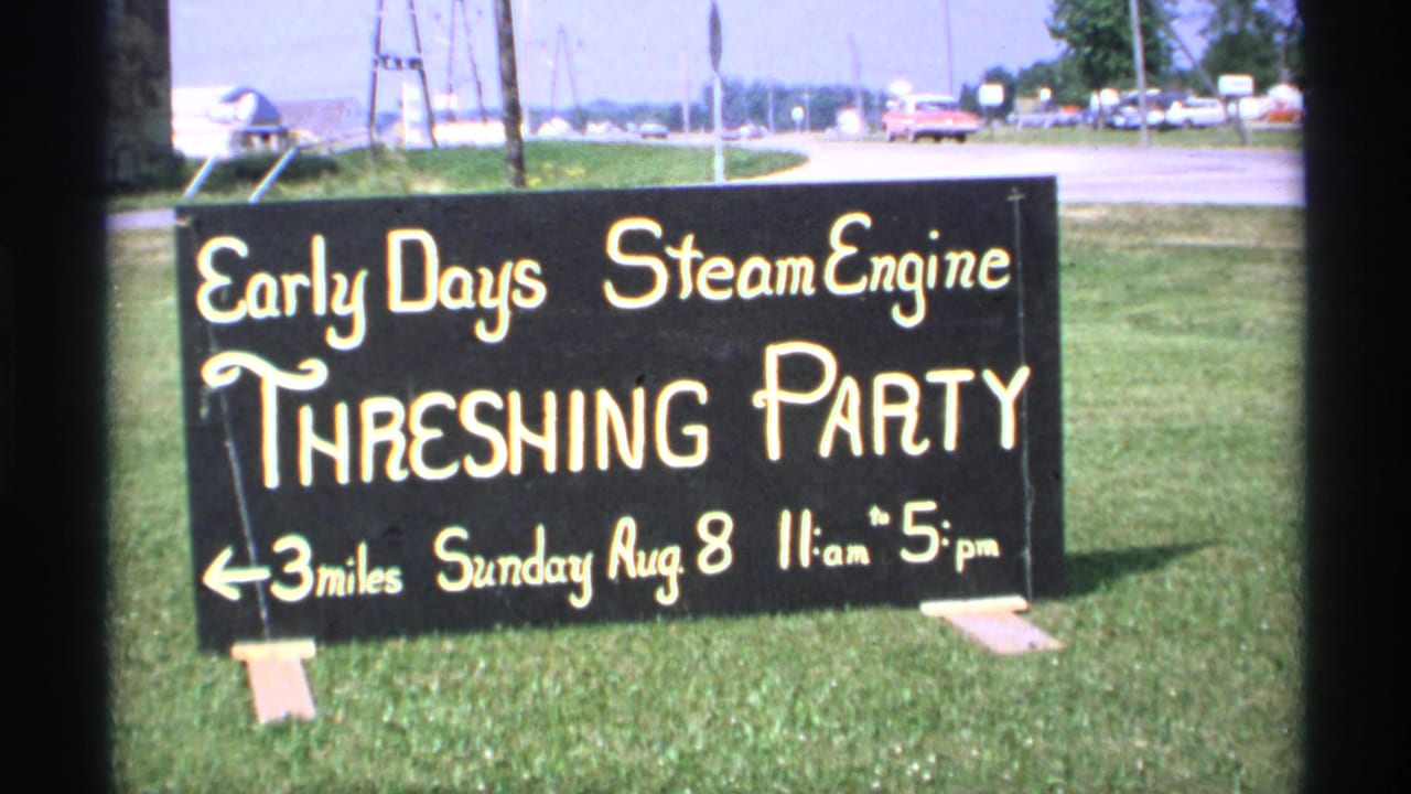 1971 Minnesota 8mm frame showing a roadside sign for the Early Days Steam Engine Threshing Party, with cars and open grass behind it.
