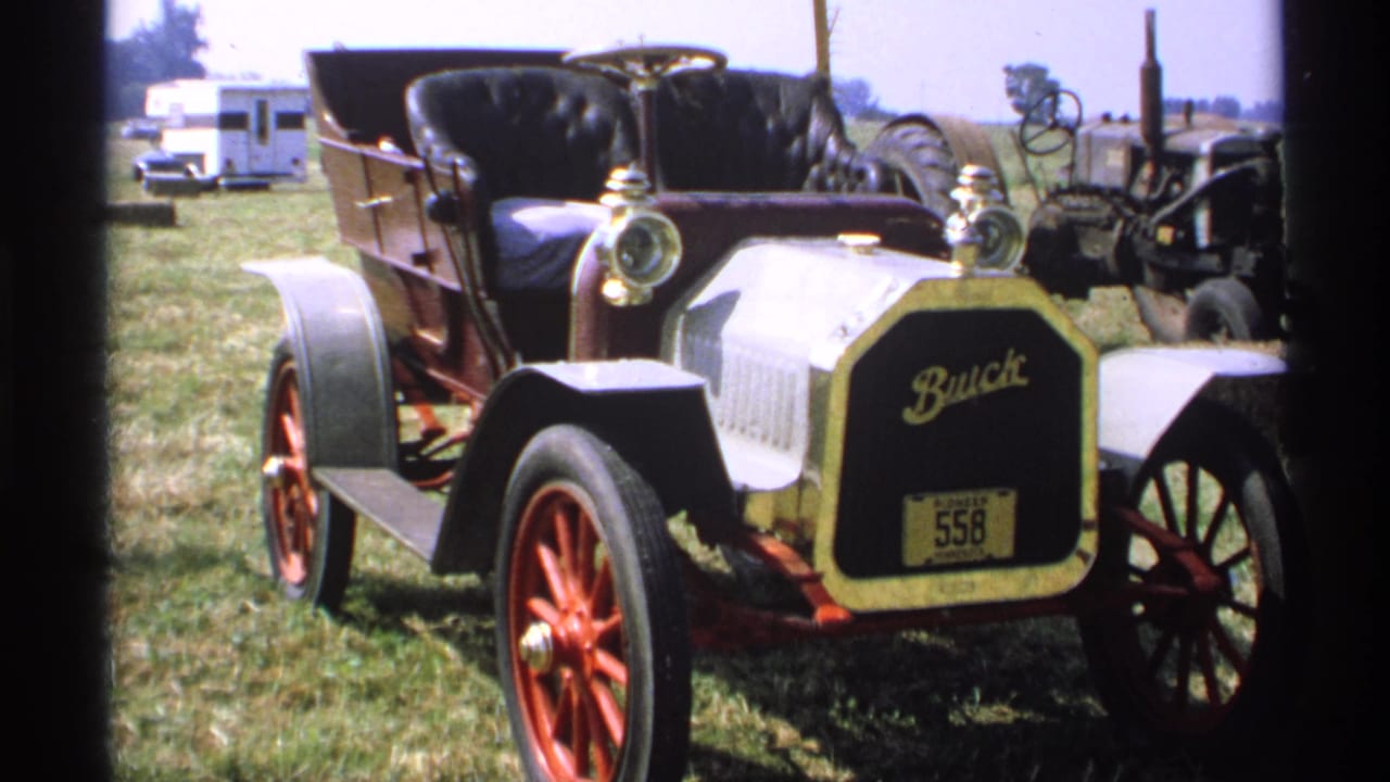The Buick display remains framed from the front, showing the badge, gold trim, red wheels, black seat, and rural fairground surroundings.