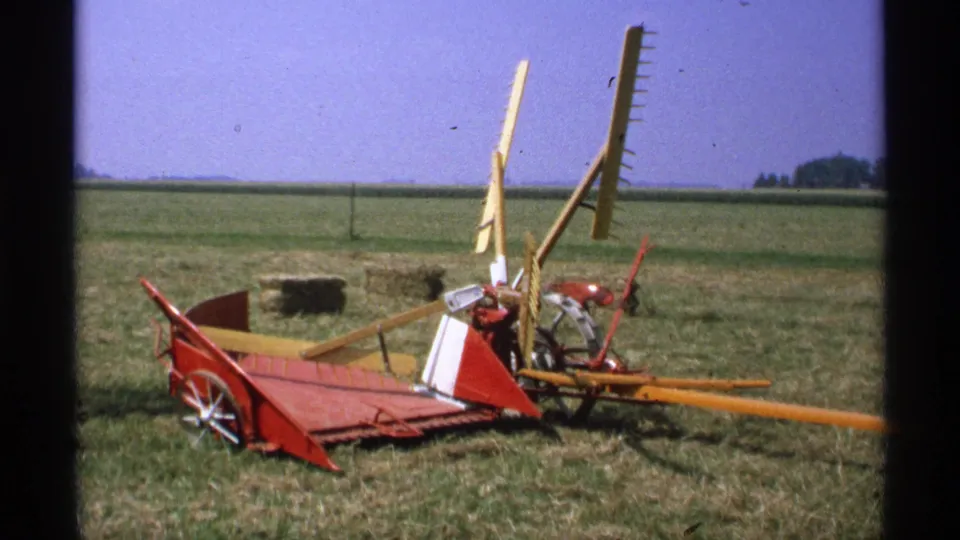 A later frame shows a red and yellow farm implement or hay rake on grass, with open fields and a clear sky in the background.