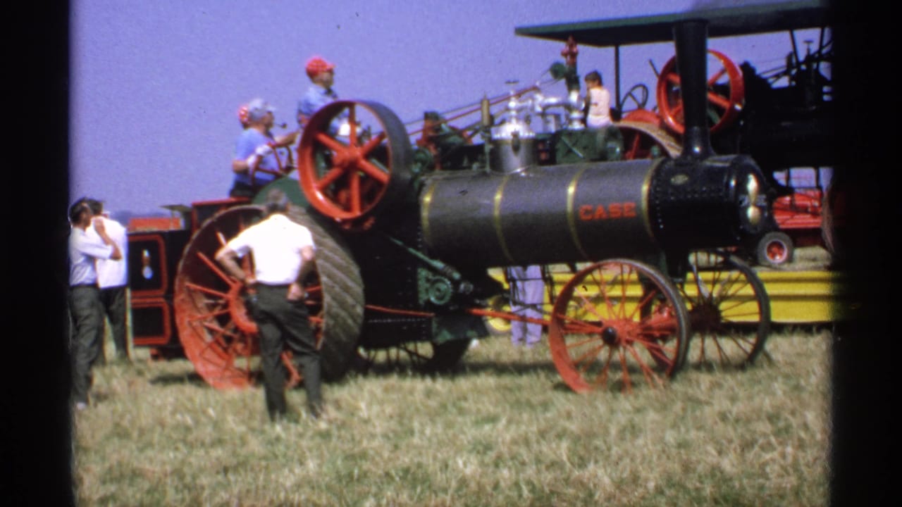 Black Case steam tractor with red wheels on a grassy fairground as adults stand nearby.