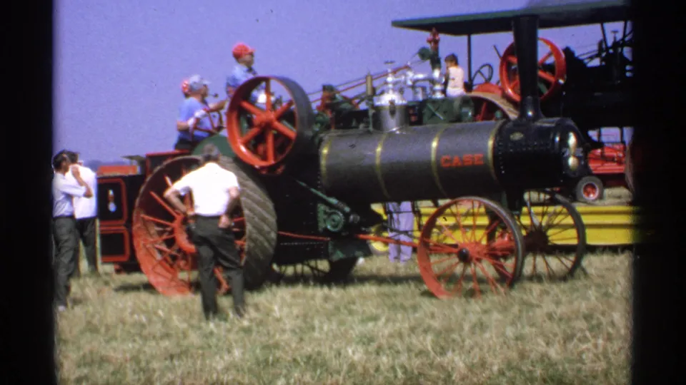 1971 Minnesota home-movie frame showing a black Case steam tractor with red wheels and fairgoers gathered beside it.
