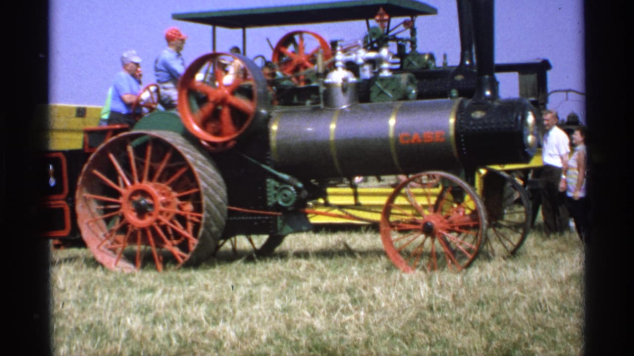 CASE steam tractor with red wheels in a grassy field, with adults seated and standing nearby.