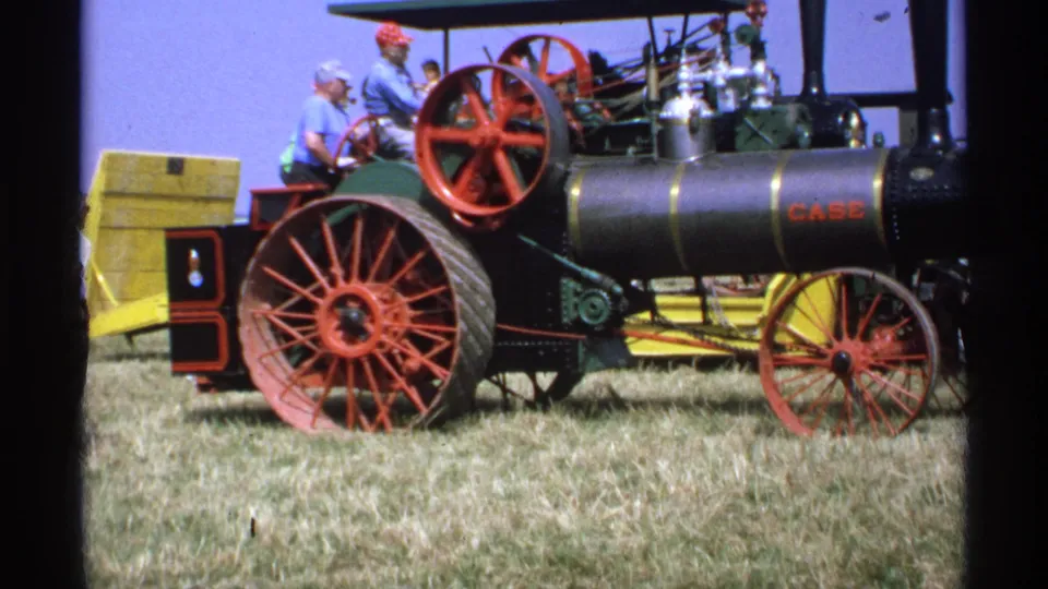 1971 Minnesota frame showing the side of a CASE steam tractor with red spoked wheels and several adults at a rural exhibition.