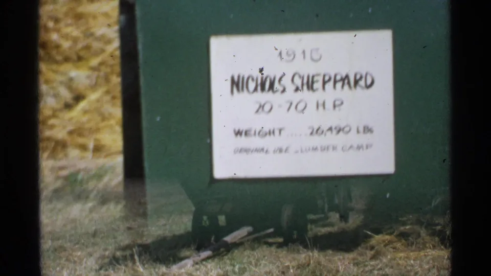 Minnesota 1971 8mm frame with the Nichols Sheppard placard on green machinery, seen near hay and field ground.
