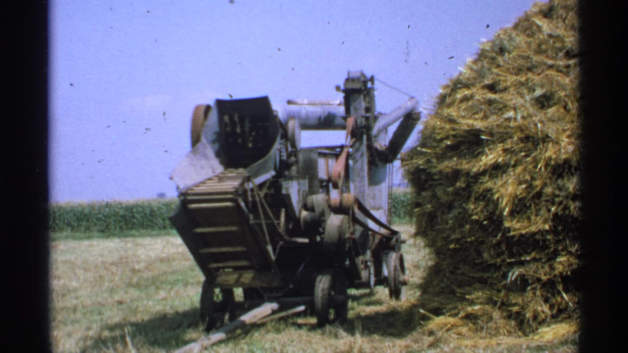 Agricultural machinery beside a large hay or straw stack in a rural field.