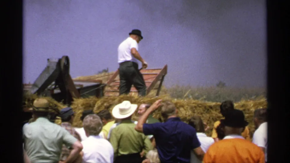 Spectators in hats and casual clothing watch a hay conveyor demonstration in rural Minnesota, 1971.