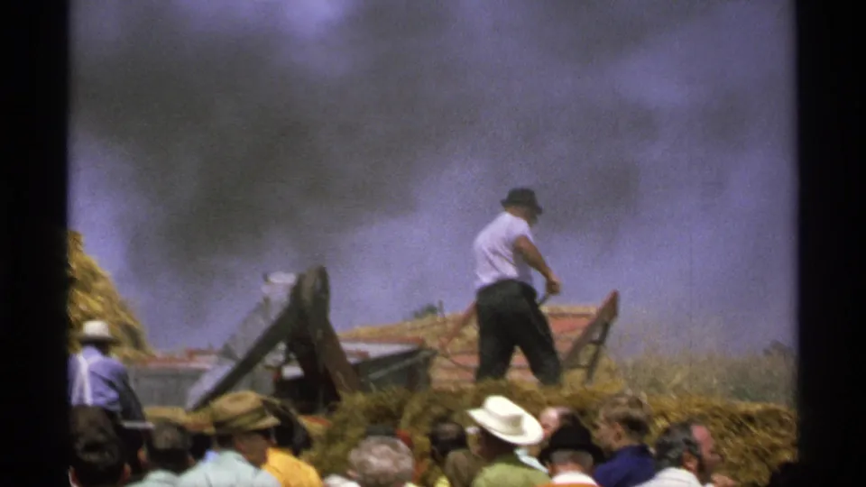 A smoky or dusty moment in the 1971 Minnesota farm demonstration shows the operator near hay and machinery with spectators in the foreground.