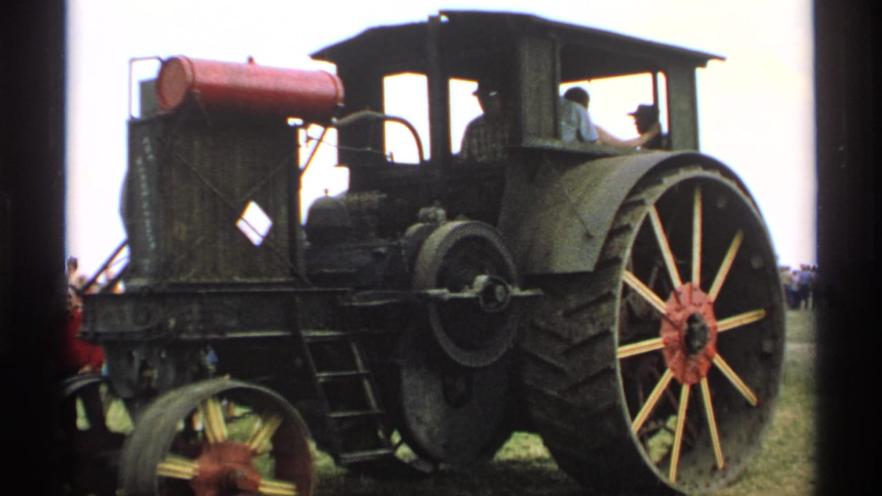 Large dark steam tractor with red tank and spoked rear wheel on a grassy field.