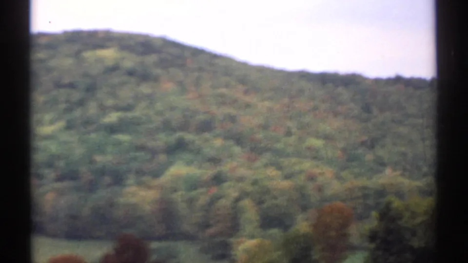 1971 New Hampshire frame with a green wooded ridge, scattered warm foliage, pale sky, and visible film gate edges.