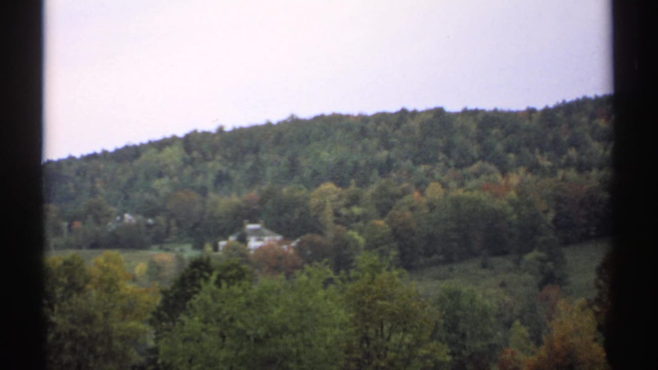 Forested New Hampshire hillside with a distant white house and dark vertical frame borders.