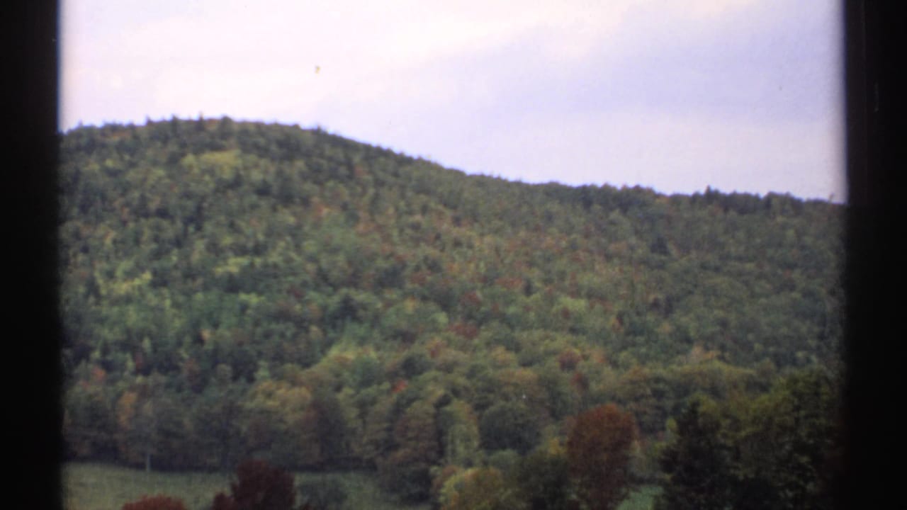 1971 8mm view of a wooded New Hampshire hillside with early autumn color, framed by dark vertical window edges.