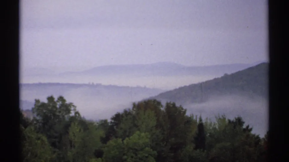 1971 New Hampshire 8mm view of a mist-filled valley with foreground trees and distant mountain ridges fading into haze.