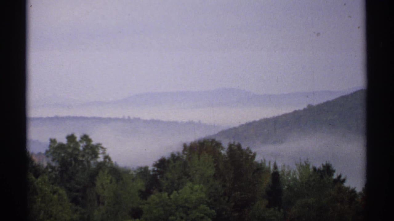1971 New Hampshire 8mm frame showing mist layered over wooded hills with dark green trees in the foreground.