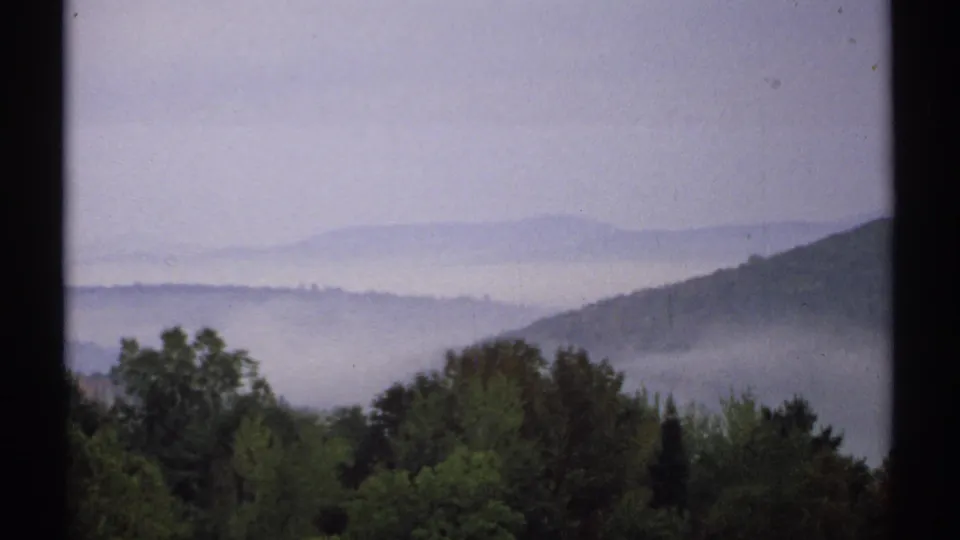 1971 New Hampshire 8mm frame showing mist layered over wooded hills with dark green trees in the foreground.