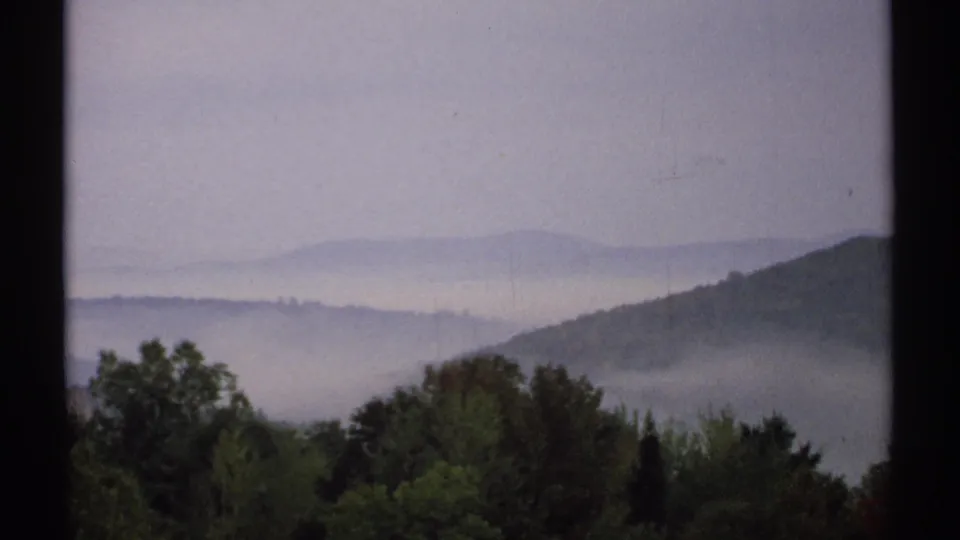1971 New Hampshire 8mm frame with wooded foreground, distant hills, and low mist across the valley.