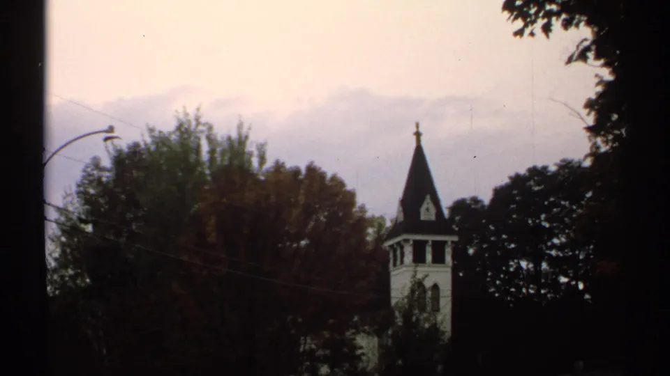 1971 New Hampshire 8mm frame showing a dark church steeple partly framed by trees against misty hills.