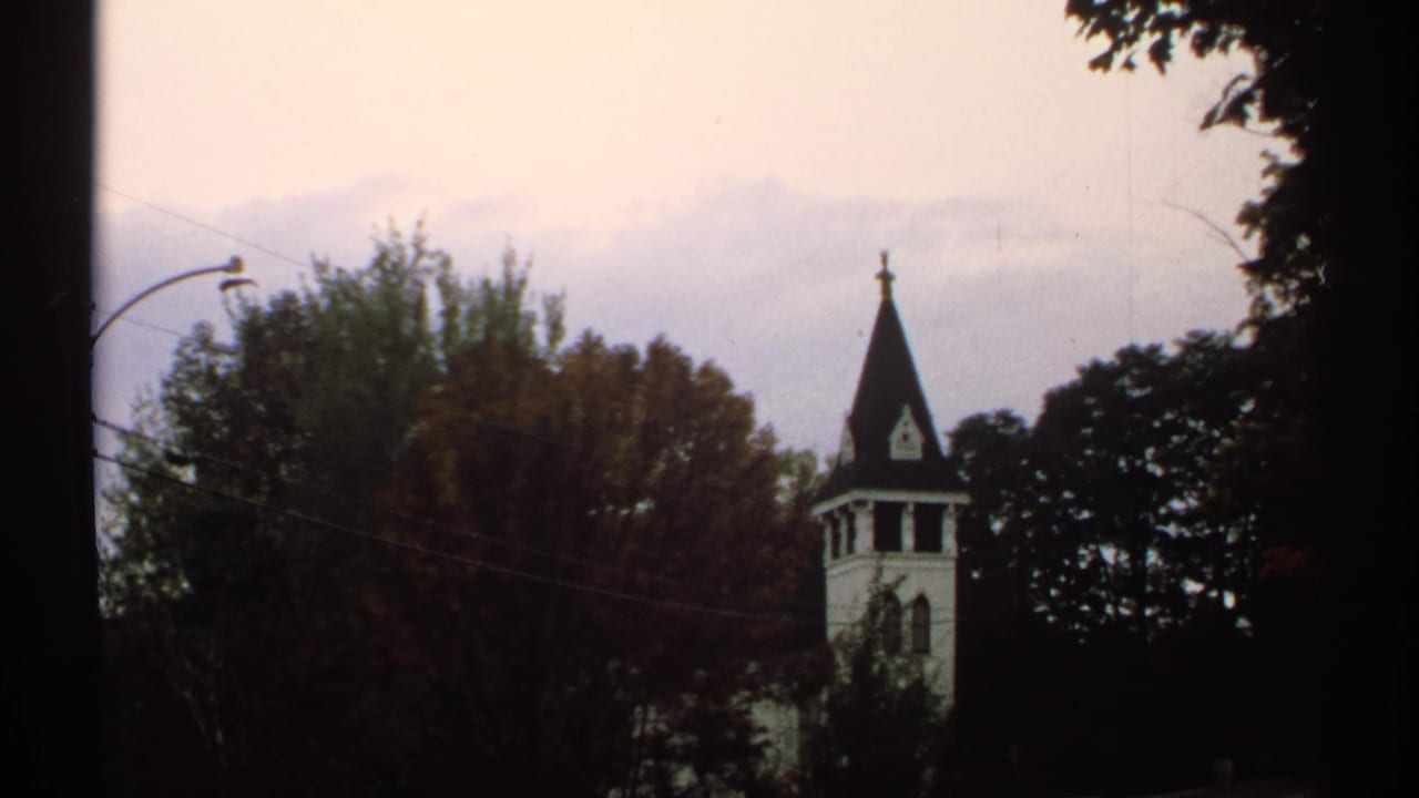 1971 New Hampshire 8mm frame of a white church steeple partly framed by autumn trees and a pale sky.