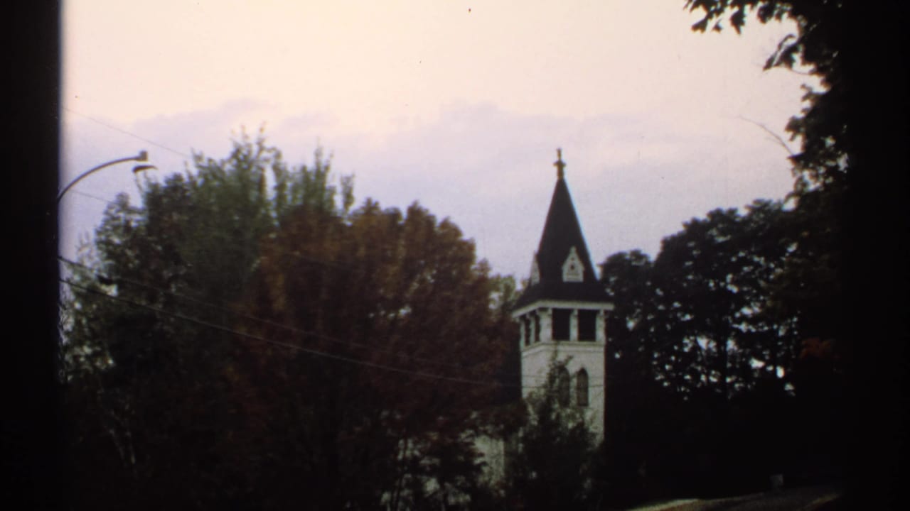 Church steeple and trees seen through soft 8mm film grain.
