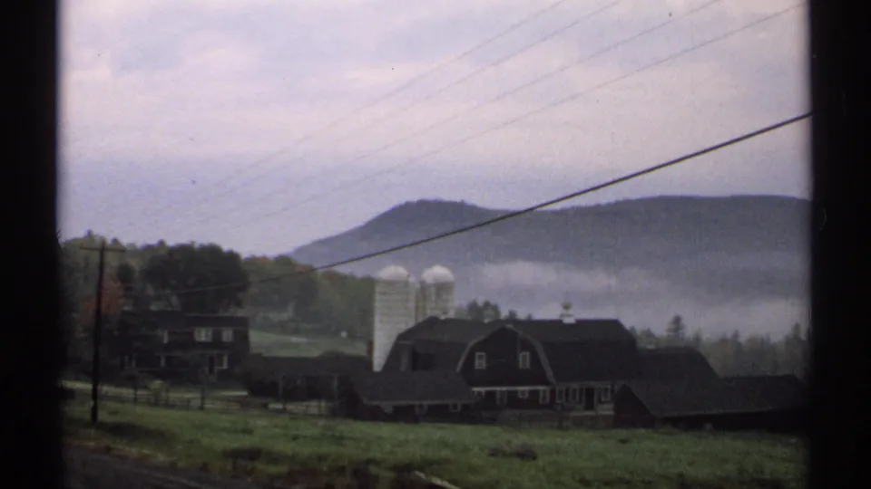 New Hampshire farm landscape from 1971 showing barns, silos, pasture, low hills, and a band of mist.