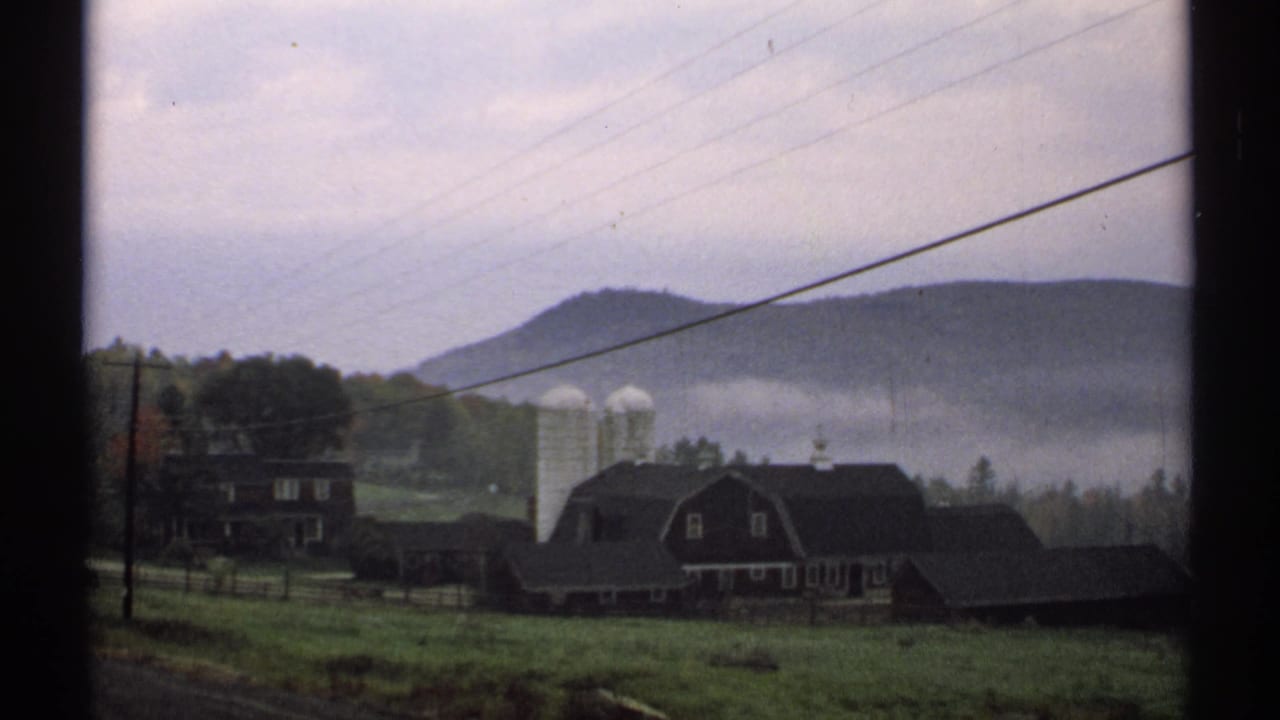 Farmhouse, silos, green field, utility wires, and misty wooded mountains.
