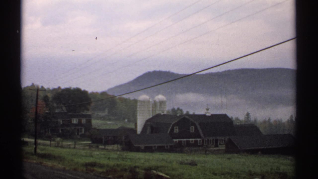Rural farmhouse and silos beneath foggy hills, crossed by overhead wires.
