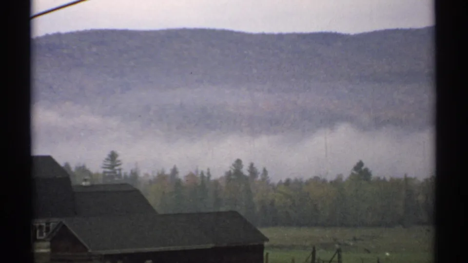 The final frame holds on farm roofs and pasture below low fog and wooded New Hampshire hills in soft 8mm color.