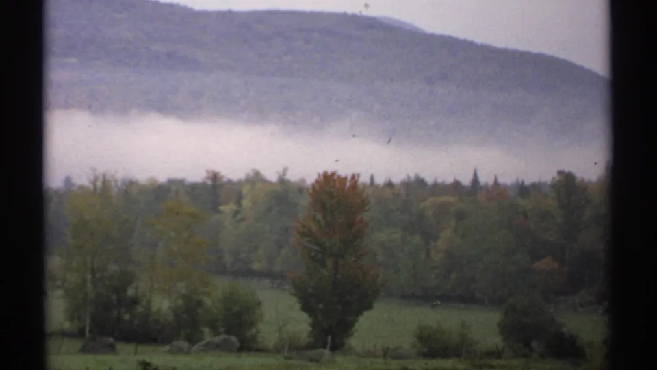 1971 New Hampshire landscape showing a fog-covered mountain base, forested valley, field, and autumn tree through a window.
