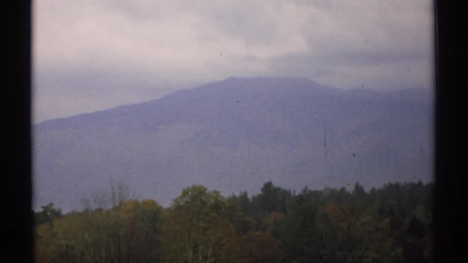 1971 New Hampshire 8mm frame with a soft blue-gray mountain silhouette above a mixed forest treeline.