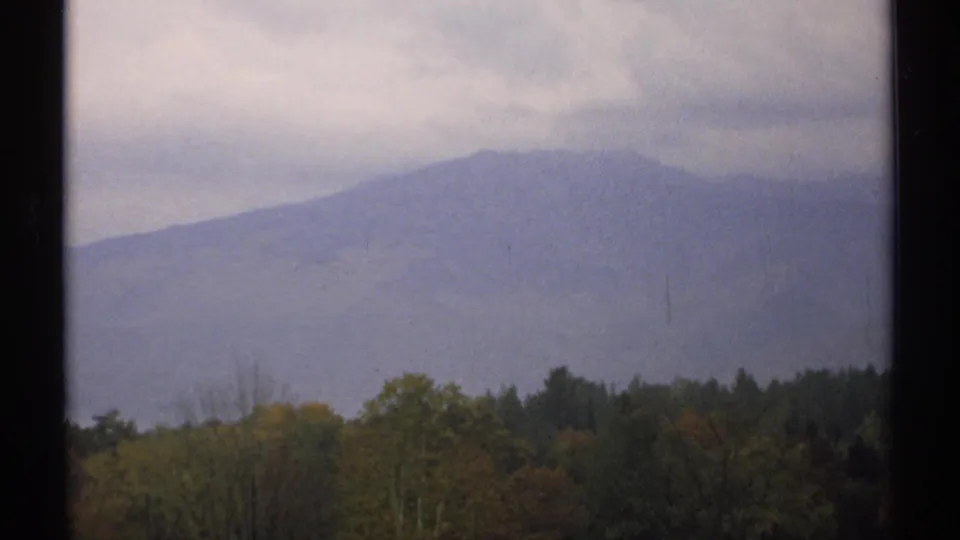 1971 New Hampshire 8mm landscape frame showing a misty ridge beyond autumn-tinted trees and evergreens.