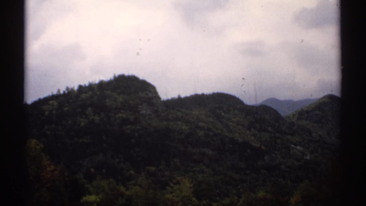 Dark wooded hill and distant ridges beneath a cloudy sky.