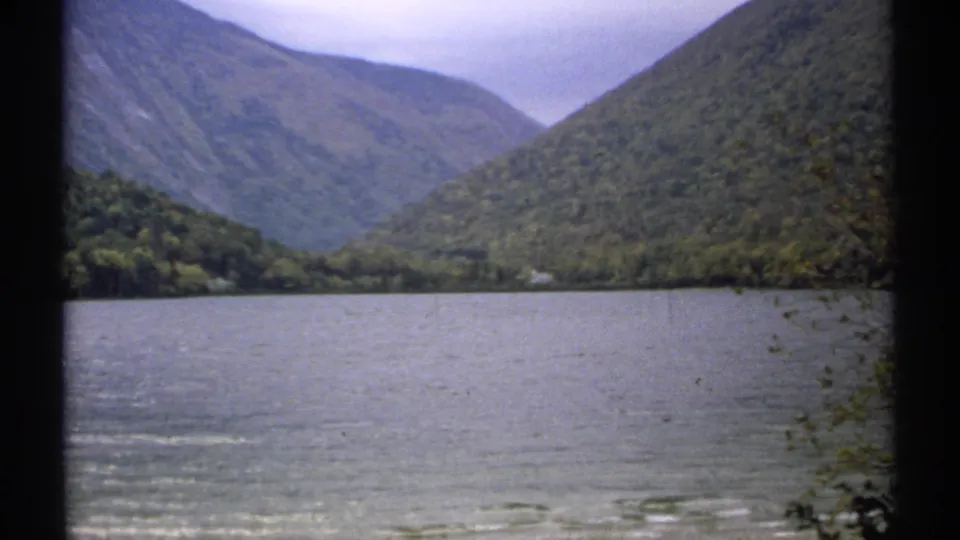 Visitor-shot 1971 New Hampshire frame of Echo Lake water, wooded banks, and layered mountain slopes in soft 8mm color.