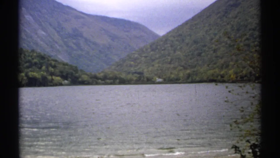 1971 New Hampshire home-movie frame holding on Echo Lake, with rippled water, forested slopes, and a muted overcast sky.