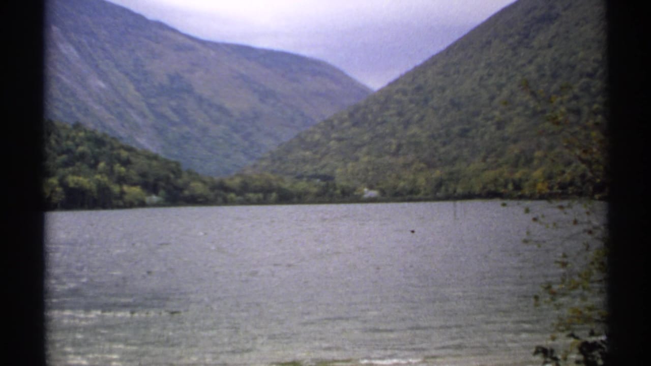 Forested mountains rising behind a calm lake with dark film borders.