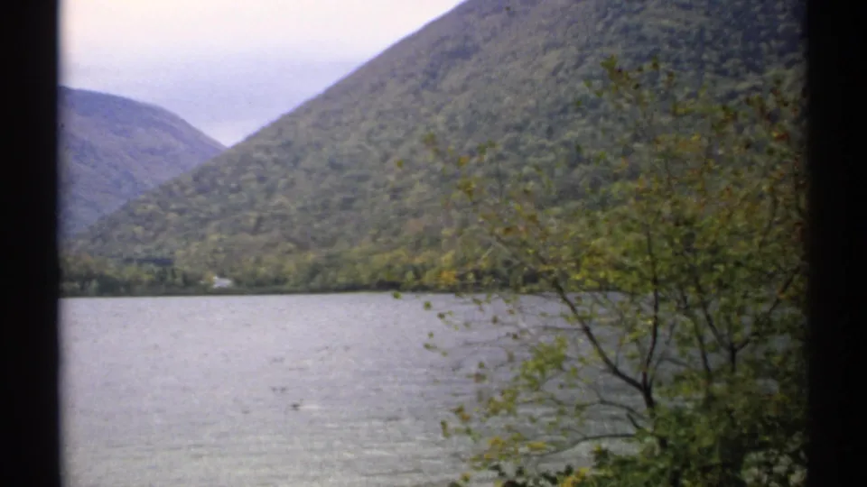 1971 New Hampshire 8mm still showing a broad lake, steep forested mountain, and autumn-tinted branches.