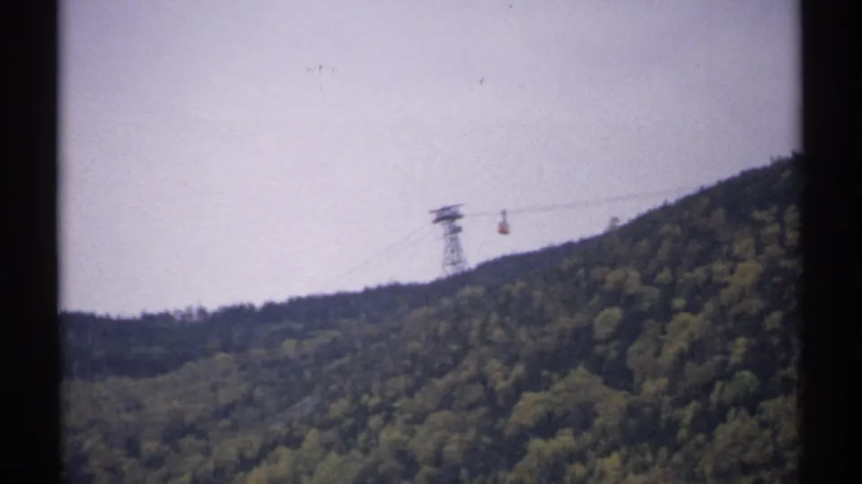1971 New Hampshire 8mm frame showing a distant aerial tramway tower and cable car over a wooded mountain ridge.